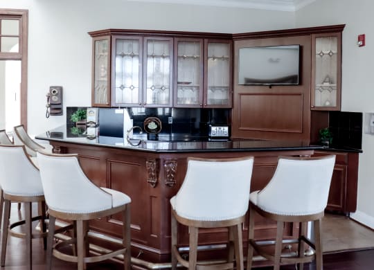 a bar with white chairs in a living room with a wooden cabinet at Broadlands Apartments in Ashburn, VA